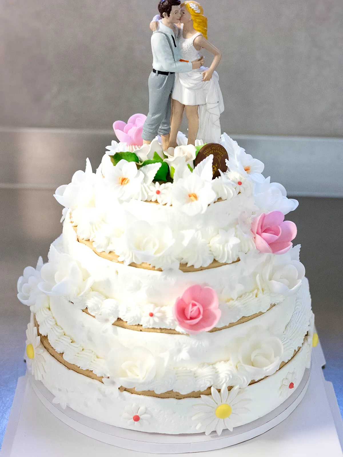 Een bruidstaart van roomijs met drie verdiepingen, witte bloemen en een bruidspaar bovenop