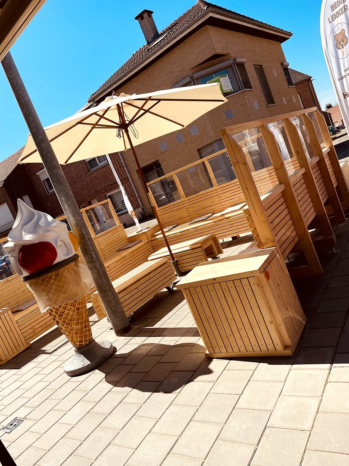 Het houten terras van Beire Lekker in de zon, met parasol en een grote ijshoorn